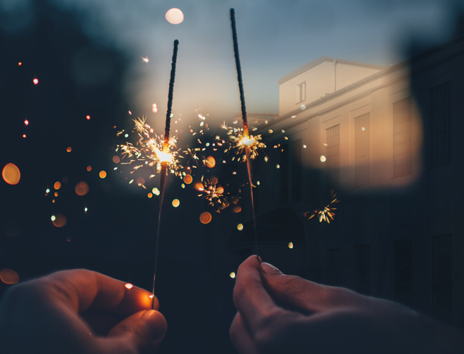 Zwei Hände halten eine leuchtende Wunderkerze vor dem OWYO CAMPUS im Hintergrund. Die Szene symbolisiert den Jahresausklang: Ruhe, Dankbarkeit für Begegnungen und Zusammenarbeit im vergangenen Jahr, sowie die Hoffnung und neuen Ideen für 2026. Ein Moment des Innehaltens zwischen den Jahren, der Wärme, Licht und Perspektiven für die Zukunft vermittelt.